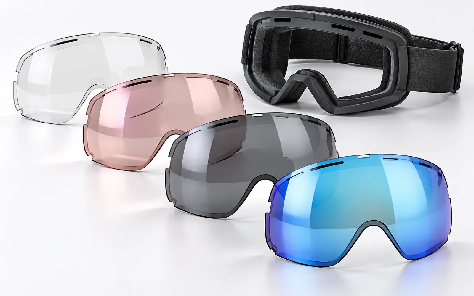 Near-clear, rose, grey and blue-mirrored replacement goggle lenses beside an empty frame